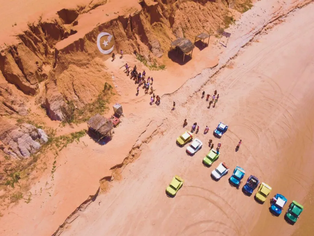 Aerial view of colorful buggies parked at the foot of the Canoa Quebrada cliffs