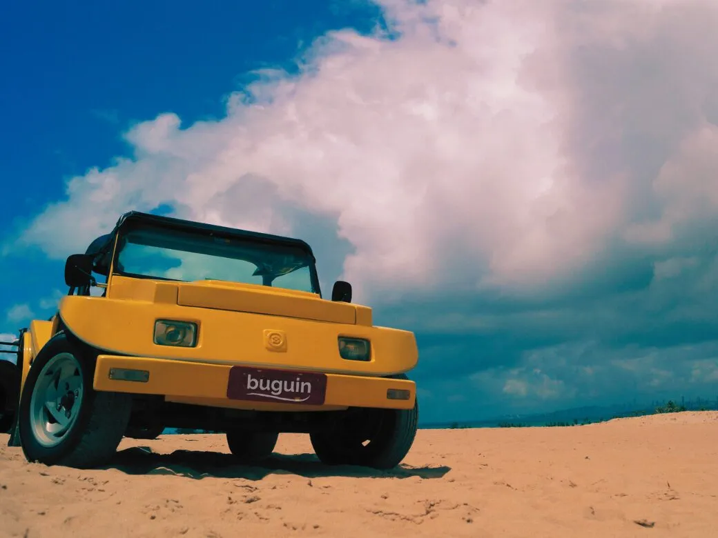 Buggy amarelo com a placa Buguin estacionado na areia sob céu azul