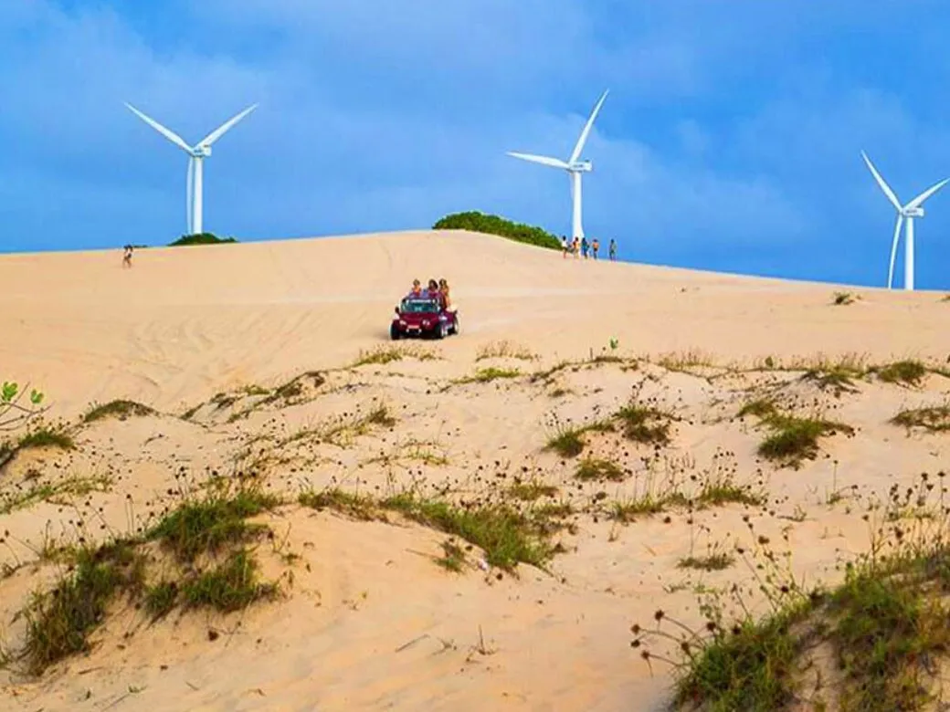 Buggy on top of a dune with wind turbines behind