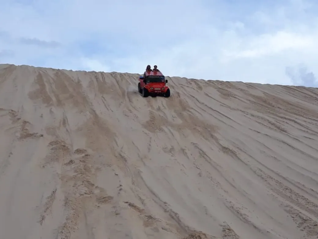Buggy climbing a tall light-sand dune under a blue sky