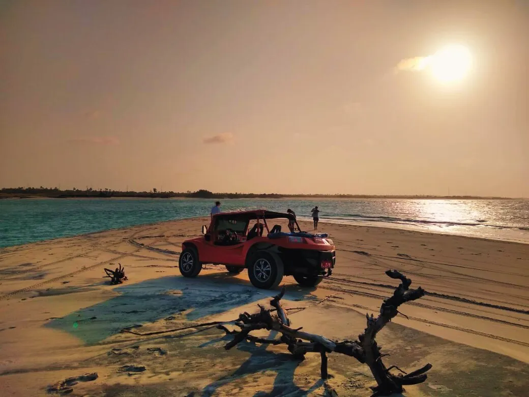 Red buggy on the beach in Fortim at sunset, with a dry tree trunk on the sand