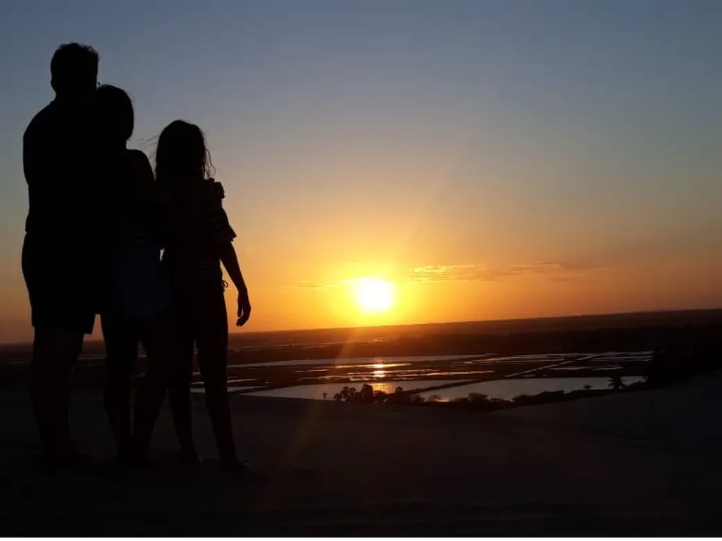 Family in silhouette watching the sunset from the top of a dune